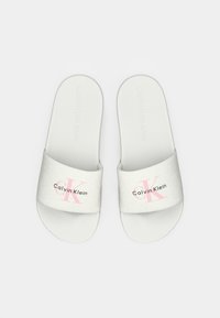 Sandali slide bianchi di Calvin Klein con logo "ck" rosa e testo "Calvin Klein" nero su ampie cinghie in tessuto, vista dall'alto su sfondo neutro.