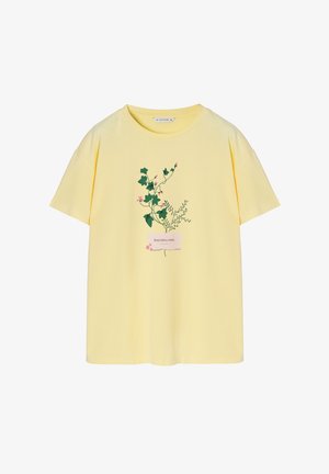 Camiseta amarilla de manga corta con un estampado floral de hiedra y acentos rosados en la parte delantera, confeccionada en tejido de algodón ligero.