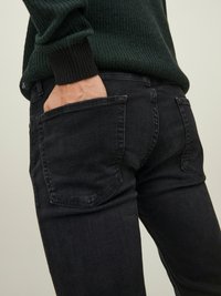 Svarte denimjeans med slim fit, med baklommer og subtile sømdetaljer, kombinert med en teksturert grønn genser.