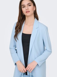 Light blue blazer with a structured design, sharp lapels, and long sleeves. Worn over a black top. Smooth texture, minimalist style.