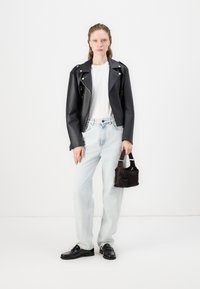 Chaqueta de motorista de cuero negra, camiseta blanca, jeans de mezclilla azul claro y mocasines negros. Sostiene un pequeño bolso de mano marrón oscuro. Diseño minimalista.