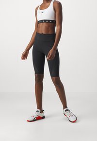 Pantaloncini atletici neri con design aderente, abbinati a un crop top bianco con fascia logo nera. Accenti testurizzati migliorano la durata.