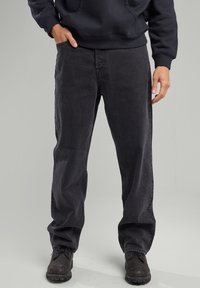 Mustat farkut, joissa on suora lahje, hienostuneella tekstuurilla ja klassisella viiden taskun tyylillä. Yhdistetty tummiin jalkineisiin.