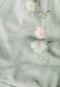 Broderat genomskinligt tyg i pastellfärger, med blommönster, som har en mjuk, lätt textur och ett delikat, svävande utseende.