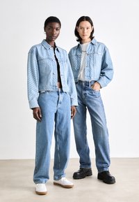 Chaquetas de mezclilla azul claro con patrones contrastantes, combinadas con jeans sueltos azules. El calzado incluye zapatillas blancas y zapatos de plataforma negros.