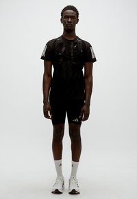 Μαύρο αθλητικό σύνολο που αποτελείται από μπλούζα με κοντά μανίκια και εφαρμοστά σορτς, με τρεις λευκές ρίγες και υφή υφάσματος.