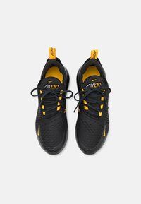 Svarta sportskor med en texturerad ovandel, gula accenter och snören. Har en rund tå och en dämpad sula för komfort.