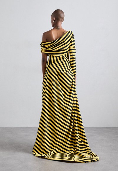 Axelklänning med asymmetrisk design, som har djärva gula och svarta ränder, fladdrande tyg och en hel längd silhuett.