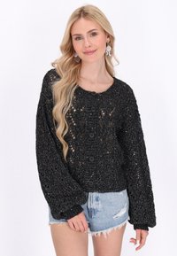 Črna odprta pletena jopica z okroglo ovratnico, dolgimi rokavi in velikimi črnimi gumbi. Nosi se čez svetlo modre denim kratke hlače.