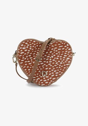 Sac bandoulière en forme de cœur avec texture pelucheuse tachetée marron et blanche, et sangle en cuir beige réglable.