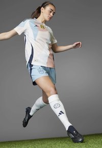 Camiseta de fútbol de España con patrones geométricos en tonos pastel, combinada con pantalones cortos azul claro y calcetines blancos, con acentos y marcas en navy.