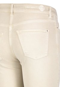 Jeans de mezclilla beige con una textura suave, que cuentan con un diseño de cinco bolsillos y costuras sutiles. La parte trasera tiene dos bolsillos de parche.