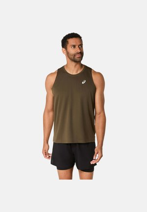 Uomo che indossa una canotta da atleta verde oliva e pantaloncini neri, in piedi davanti a uno sfondo chiaro uniforme, che guarda di lato.