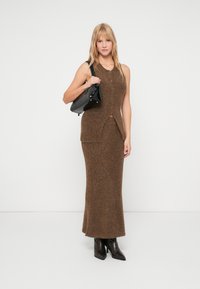 Robe-jupe en tricot marron avec décolleté rond, fermeture devant par boutons et fente sur le côté, associée à un sac à main noir et des bottes noires jusqu'aux genoux.