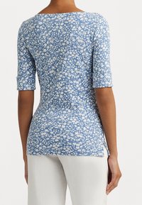 Blå blommig topp med rund halsringning, trekvartslånga upprullade ärmar och sidoklyftor. Tillverkad av ett mjukt, lätt material.