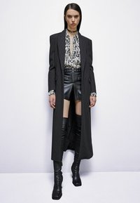 Abrigo largo a rayas, blusa estampada, pantalones cortos de cuero y botas altas. Paleta de colores negra con texturas y acentos distintivos.
