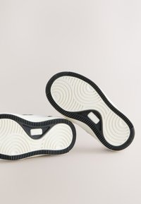 Black and white sneakers with circular patterned soles positioned sole-up on a neutral background.