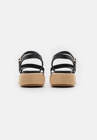 Czarne skórzane sandały z wieloma krzyżującymi się paskami, beżową plecioną platformą o fakturowanej powierzchni oraz małą złotą klamrą.