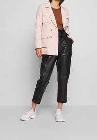 Blazer de doble botonadura en rosa claro con bolsillos frontales, combinado con pantalones de cuero negros de cintura alta y zapatillas blancas.