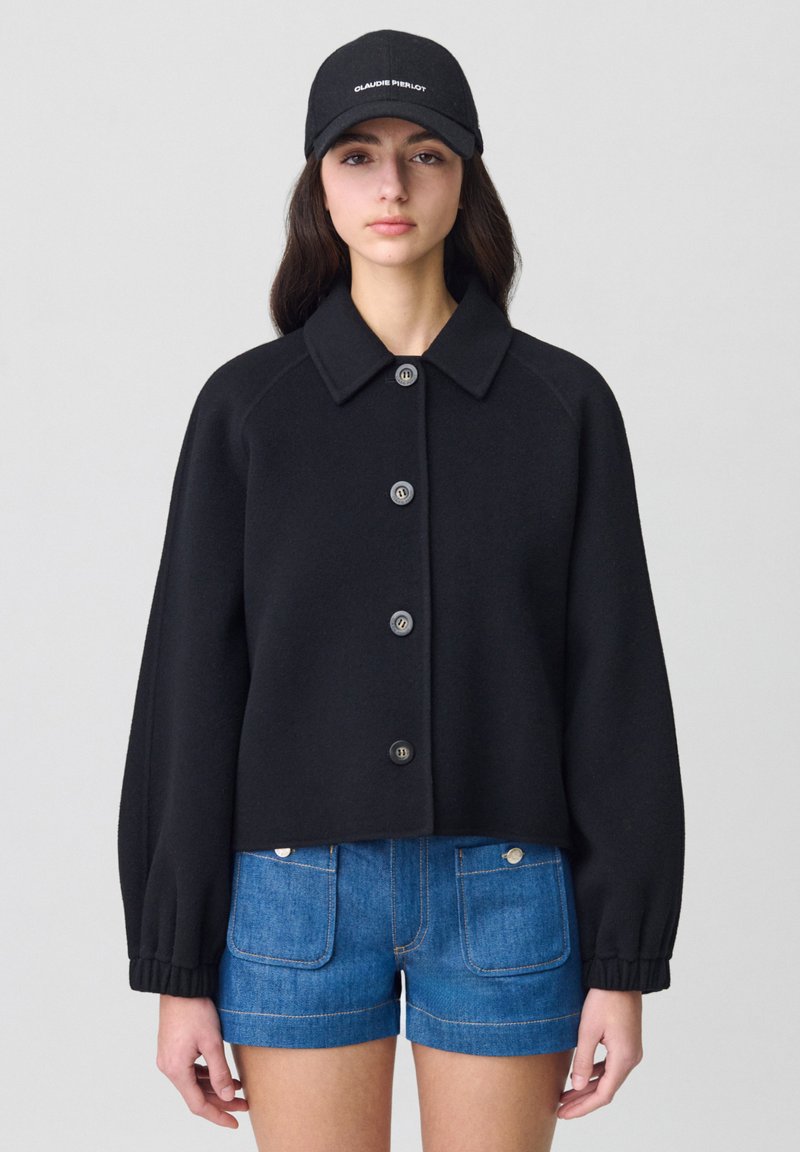 Veste noire courte avec un col et cinq boutons, associée à un short en denim bleu avec des poches avant et des accents de boutons.