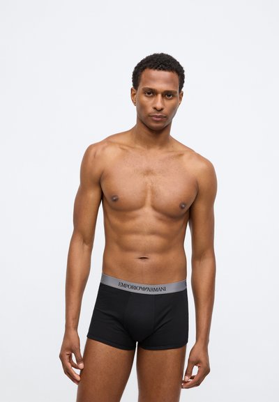 Μαύρο βαμβακερό μποξεράκι με γκρι ελαστική μέση που φέρει το λογότυπο "EMPORIO ARMANI" εμπρός. Το μοντέλο εμφανίζεται χωρίς πουκάμισο.