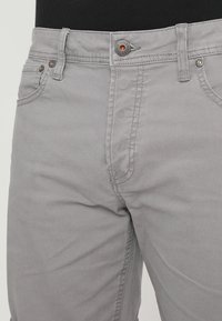 Vaaleat harmaat puuvillahousut, joissa on slim fit -leikkaus, viisi taskua, nappikiinnitys sekä kontrastiväriset ompeleet ja varusteet.