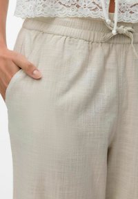 Lichtbeige, gestructureerde broek met een elastische tailleband en koord. Voorzien van zijzakken en een losse pasvorm.