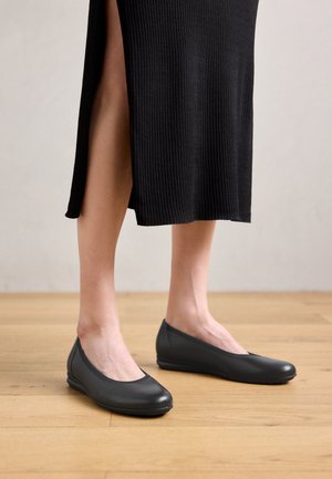 Gray ballet flats with a sleek design, rounded toe, and smooth leather texture, paired with a black ribbed dress featuring a side slit.