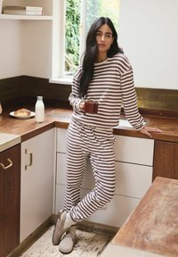 Striped, brown and white loungewear set featuring a long-sleeve top and matching pants. Accessories include a brown mug and soft slippers.
