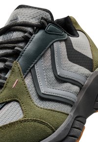 Grå och grön sneaker med en texturerad tygöverdel, läderdetaljer, geometriska designelement och en slitstark gummisula.