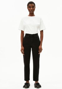 Jean noir taille haute à jambe droite, associé à un t-shirt blanc ample. La tenue présente un design minimaliste et une texture lisse.