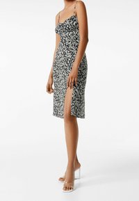 Abito floreale in bianco e nero con spalline sottili, corpino aderente e uno spacco laterale, realizzato in tessuto leggero per un silhouette fluida.