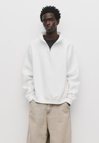 Witte zip-up sweatshirt met een hoge kraag, met een relaxte pasvorm en geribde manchetten, gecombineerd met lichtbeige broeken.