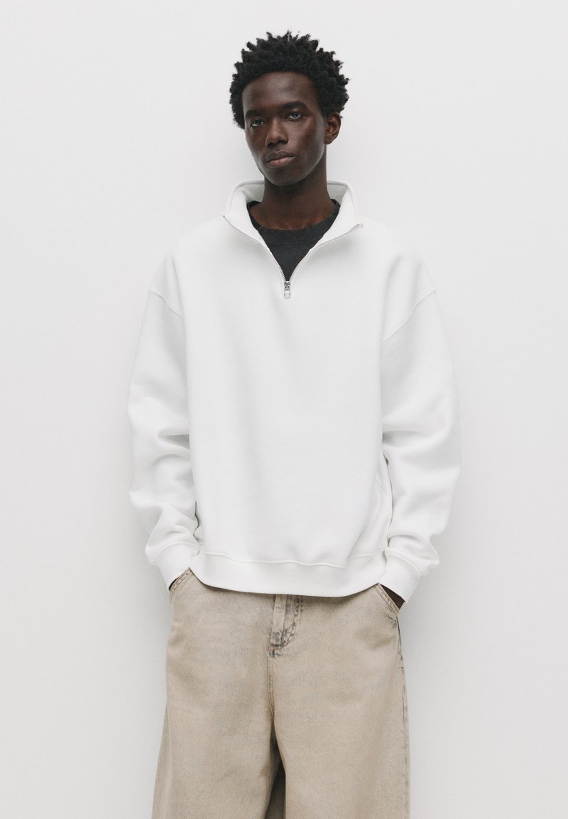Witte zip-up sweatshirt met een hoge kraag, met een relaxte pasvorm en geribde manchetten, gecombineerd met lichtbeige broeken.