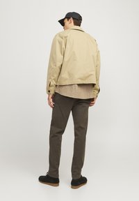 Light beige jacket with a relaxed fit, crafted from smooth fabric. Paired with a grey checkered shirt and olive green pants. Black shoes.