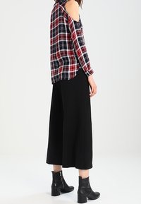 Röd och marinblå rutigt kallaxeltröja med långa ärmar, kombinerad med svarta vida byxor. Svarta ankelboots med texturerad finish.