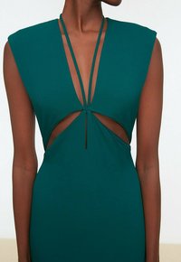 Robe découpée couleur sarcelle avec un décolleté plongeant, des épaules structurées, des bretelles fines et un tissu lisse et extensible.