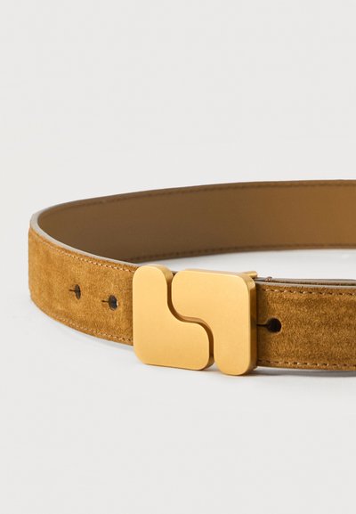 Καφέ σουέτ ζώνη με μια μεγάλη ματ χρυσή γεωμετρική πόρπη, που διαθέτει τετράγωνα σχήματα και τρεις ορατές τρύπες στη ζώνη σε λευκό φόντο.