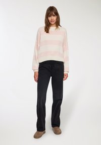 Jasnoróżowy i kremowy sweter w paski o oversize'owym kroju, czarne proste dżinsy oraz brązowe zamszowe buty. Prosty, luźny design z prążkowanymi mankietami.