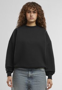 Felpa nera con collo rotondo, vestibilità oversized, spalle cadute e maniche lunghe. Abbinata a jeans in denim chiaro.