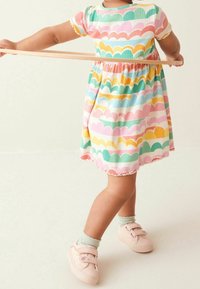 Robe colorée avec un motif en forme de vagues en rose, vert, jaune et bleu ; manches courtes, taille froncée et ourlet en étages. Baskets roses avec des bandes velcro.