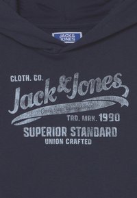 Navy blue hoodie with a front print in silver featuring "Jack & Jones," "Superior Standard," and "Union Crafted." Smooth fabric texture.