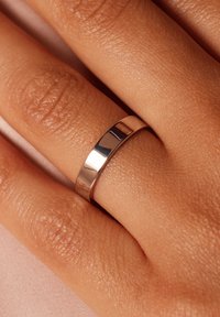Polierter Silberring an einer Hand, mit einem glatten, flachen Design des Rings. Die Oberfläche reflektiert Licht und betont ihre elegante Textur.