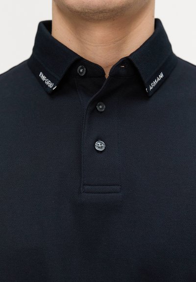 Marinblå polo med en texturerad väv, knappstängning och en kontrasterande krage med "Emporio Armani"-logotyp.