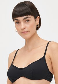 Top bikini nero con spalline sottili, caratterizzato da un design strutturato e senza cuciture in tessuto morbido. Stile minimalista senza motivi o decorazioni.
