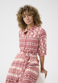 Abito camicia stampato in tonalità di rosa e crema, con maniche corte, cintura in vita e intricate motivi geometrici su tutta la superficie.