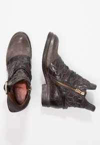 Bruine leren enkellaarsjes met een textuur van geometrische patronen, een decoratieve ritssluiting en een stevige hak. Voorzien van een contrasterende band over de voorkant.