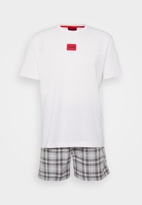 Biela bavlnená T-shirt s červeným štvorcovým logom, skombinovaná so šedými a čiernymi károvanými šortkami s elastickým pásom a voľným strihom.