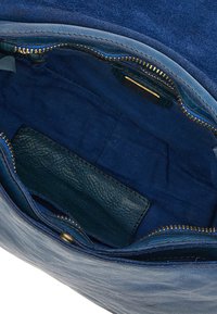 Interno di una borsa in suede blu che mostra una tasca in pelle liscia, una cerniera dorata e una fodera in tessuto testurizzato. Bordature cucite visibili.