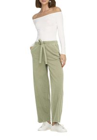 Pantaloni a palazzo verde chiaro con vita regolabile, realizzati in tessuto morbido, abbinati a una blusa bianca scollata sulle spalle e sneakers bianche.